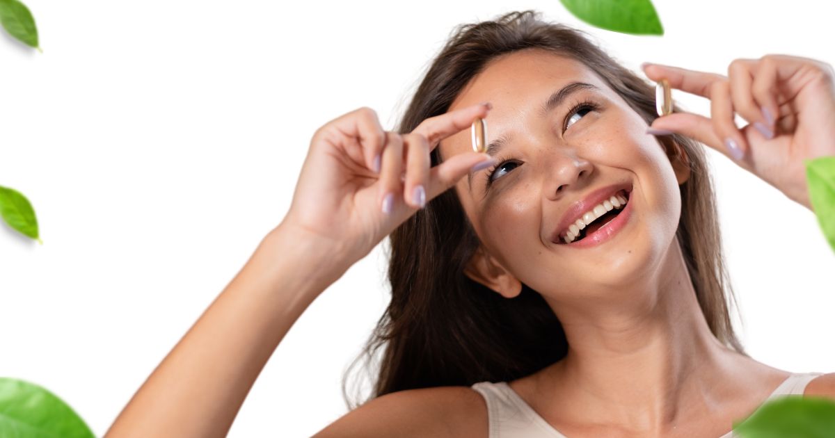 Smiling woman holding two capsules up near her eyes, suggesting she is taking vitamins or supplements.